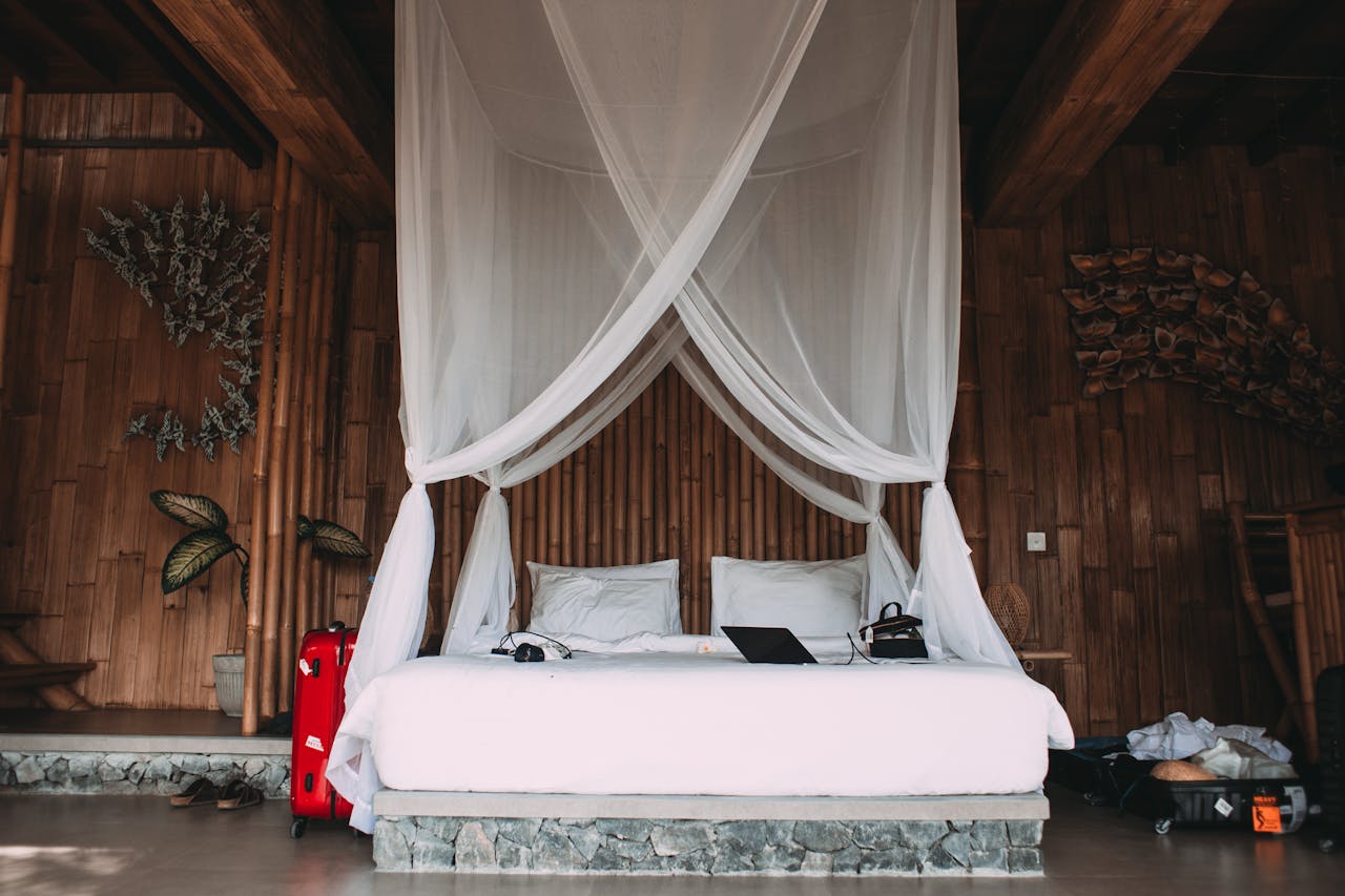About Comfortable bed with netbook and headphones near suitcases and bamboo walls in hotel room